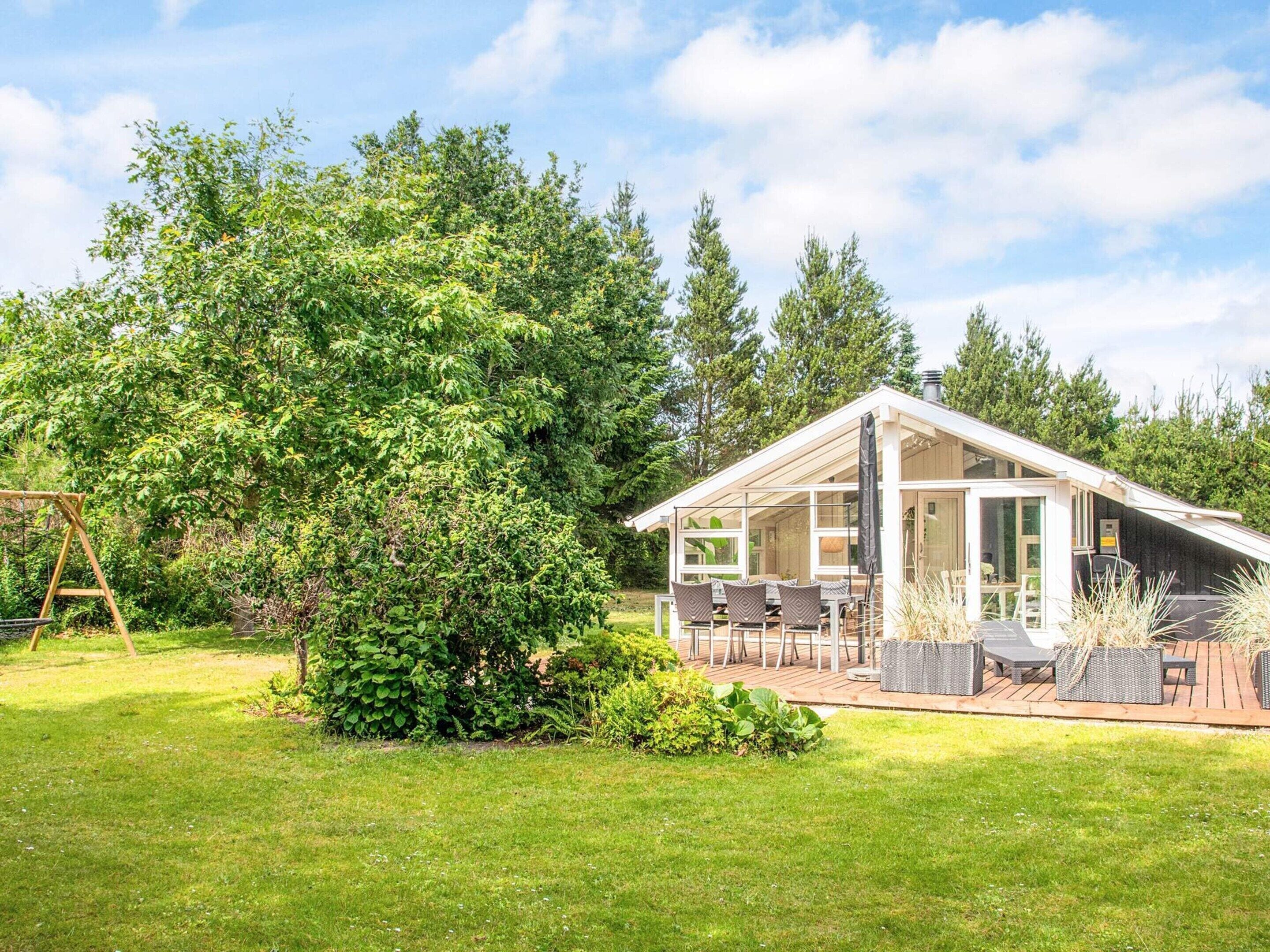 A modern house with a patio area, a swing set, and a large tree.