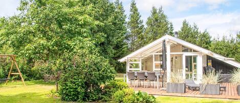 A modern house with a patio area, a swing set, and a large tree.