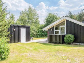 A small, single-story building with a dark exterior, a white door, and a window. - 6 Person Holiday Home in Ulfborg (Ulfborg)