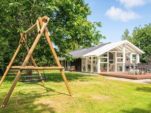 A wooden swing set in a grassy yard with a house featuring large windows and a deck. - 6 Person Holiday Home in Ulfborg (Ulfborg)
