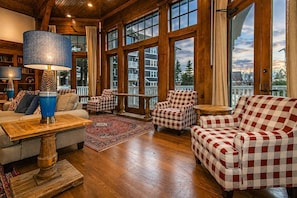 A spacious living room with a large window, a checkered sofa, a wooden coffee table, and a lamp. - AS 111 - Summer Comfort with a View & Pool Facing Village Escape (Snowshoe)