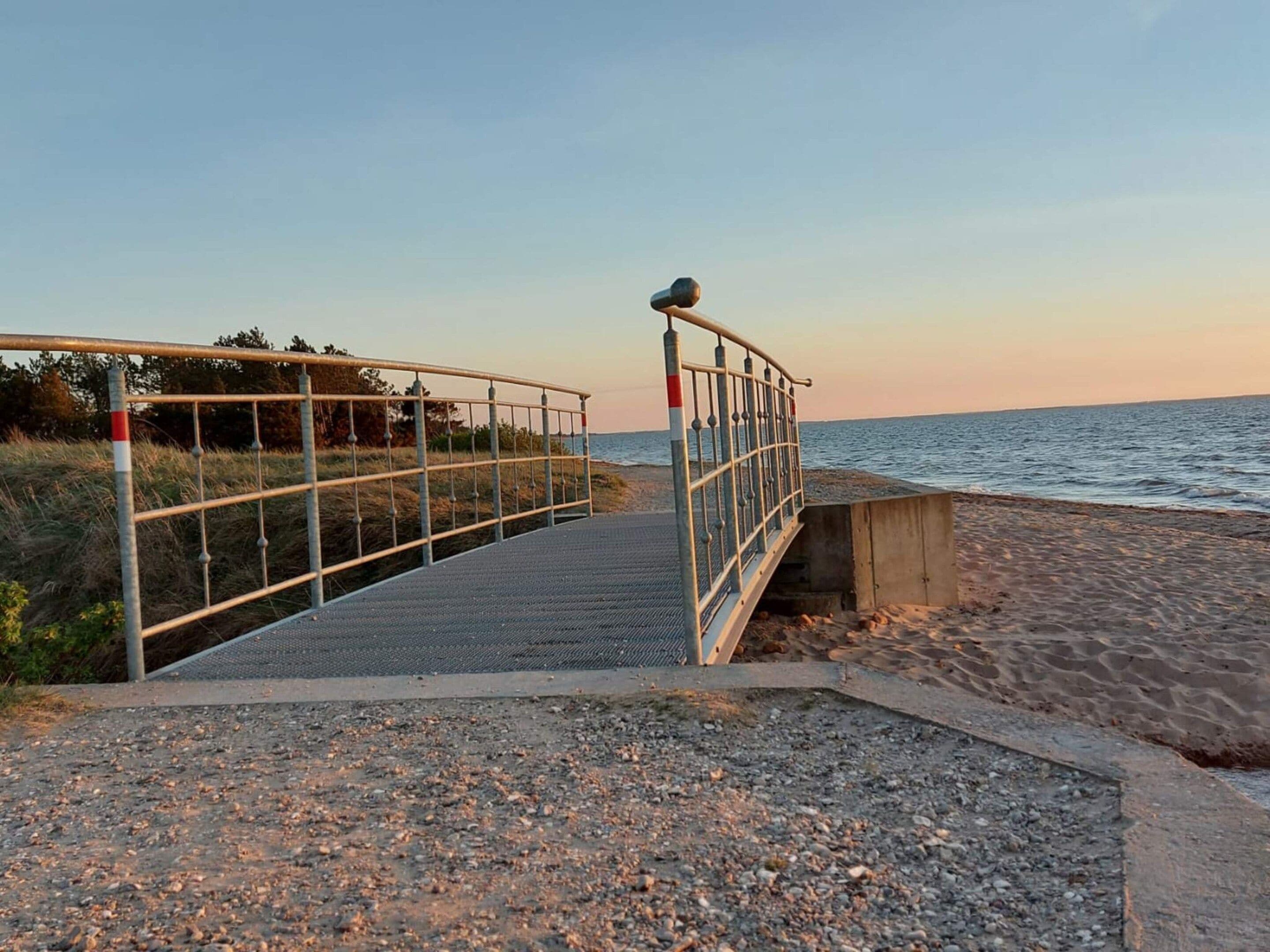 En kyststi der fører ned til havet, med gelænder og betondæmpning.