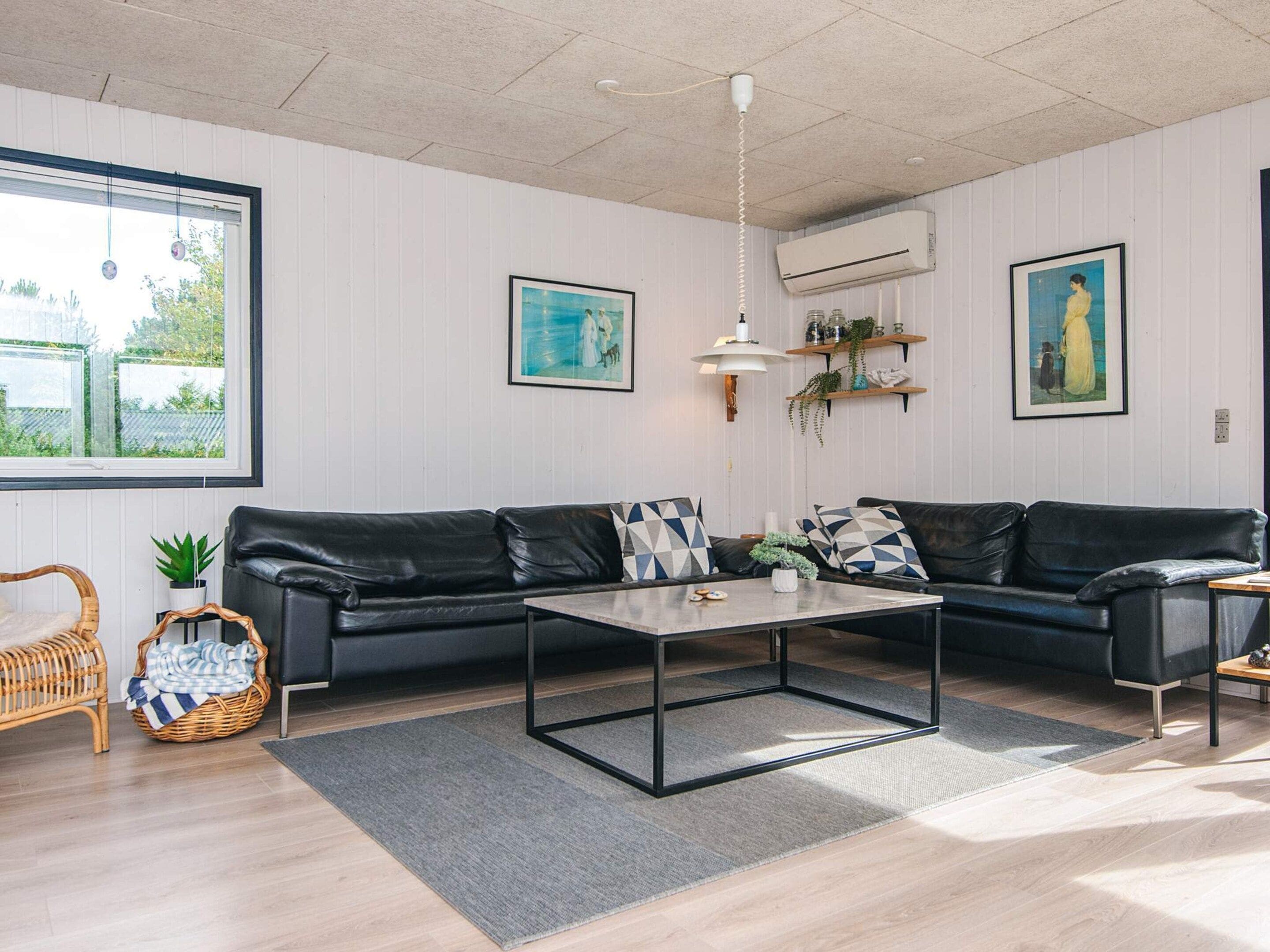 Uma sala de estar moderna com um sofá de couro preto, uma mesa de centro de madeira e uma janela grande com vista para o verde.