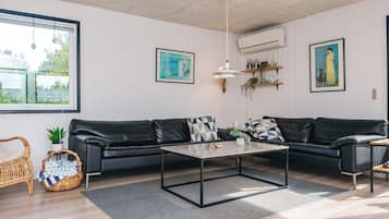 Uma sala de estar moderna com um sofá de couro preto, uma mesa de centro de madeira e uma janela grande com vista para o verde.