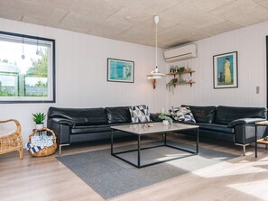 A modern living room with a black leather sofa, a wooden coffee table, and a large window with a view of greenery. - 6 Person Holiday Home in Tarm (Tarm)