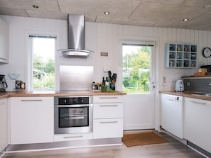 A modern kitchen with white cabinetry, stainless steel appliances, and a view of greenery outside.