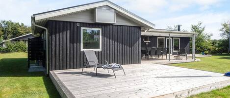 Ein modernes Haus mit einer Holzterrasse, einer überdachten Veranda und einem großen Fenster.