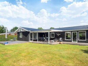 Une maison moderne dotée d’un patio couvert, de grandes fenêtres et d’une pelouse bien entretenue.