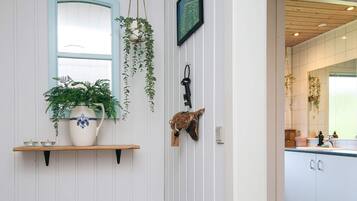 Quarto com parede branca, janela emoldurada em azul, prateleira com planta em vaso, chave pendurada e porta-chaves rústico.