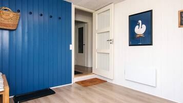 Un pasillo con una pared azul, una puerta blanca, un cuadro de un cisne enmarcado y un bolso tejido en la pared.