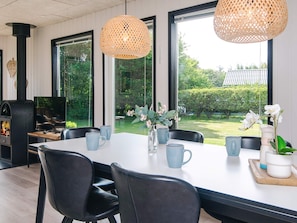 A modern dining area with a large table, black chairs, and wicker pendant lights. A fireplace and a television are visible in the background. - 6 Person Holiday Home in Tarm (Tarm)