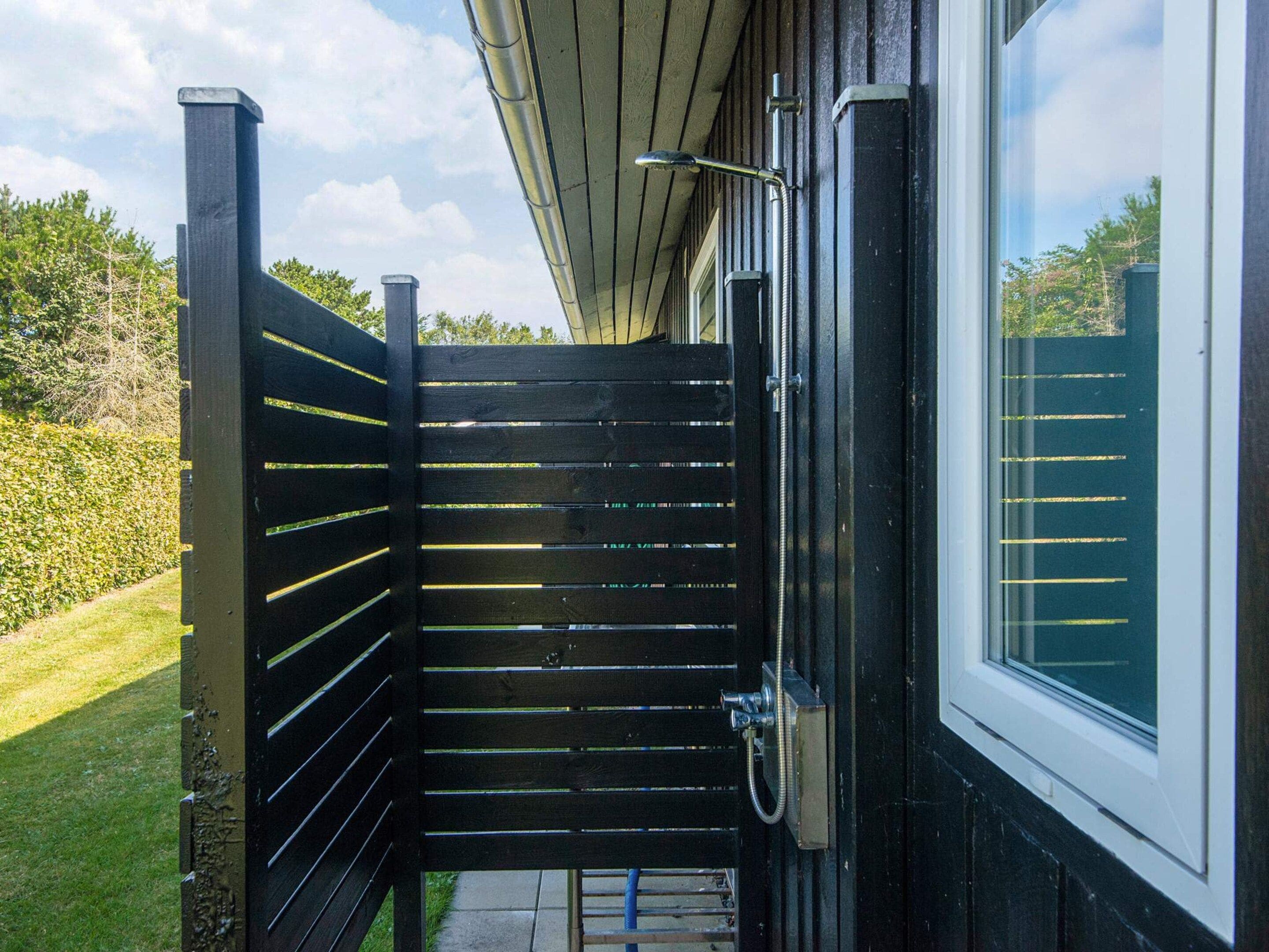 A black metal gate leading to a building with a window and a hose on the right side.