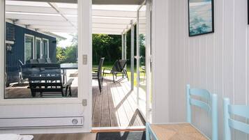 Una habitación con piso de madera, una cama, una ventana y una puerta que da a una terraza exterior con una mesa y sillas.