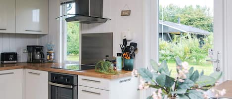 Een moderne keuken met witte kasten, een roestvrijstalen afzuigkap en uitzicht op een huis door een groot raam.