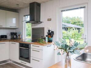 A modern kitchen with white cabinets, a stainless steel range hood, and a view of a house through a large window. - 6 Person Holiday Home in Tarm (Tarm)