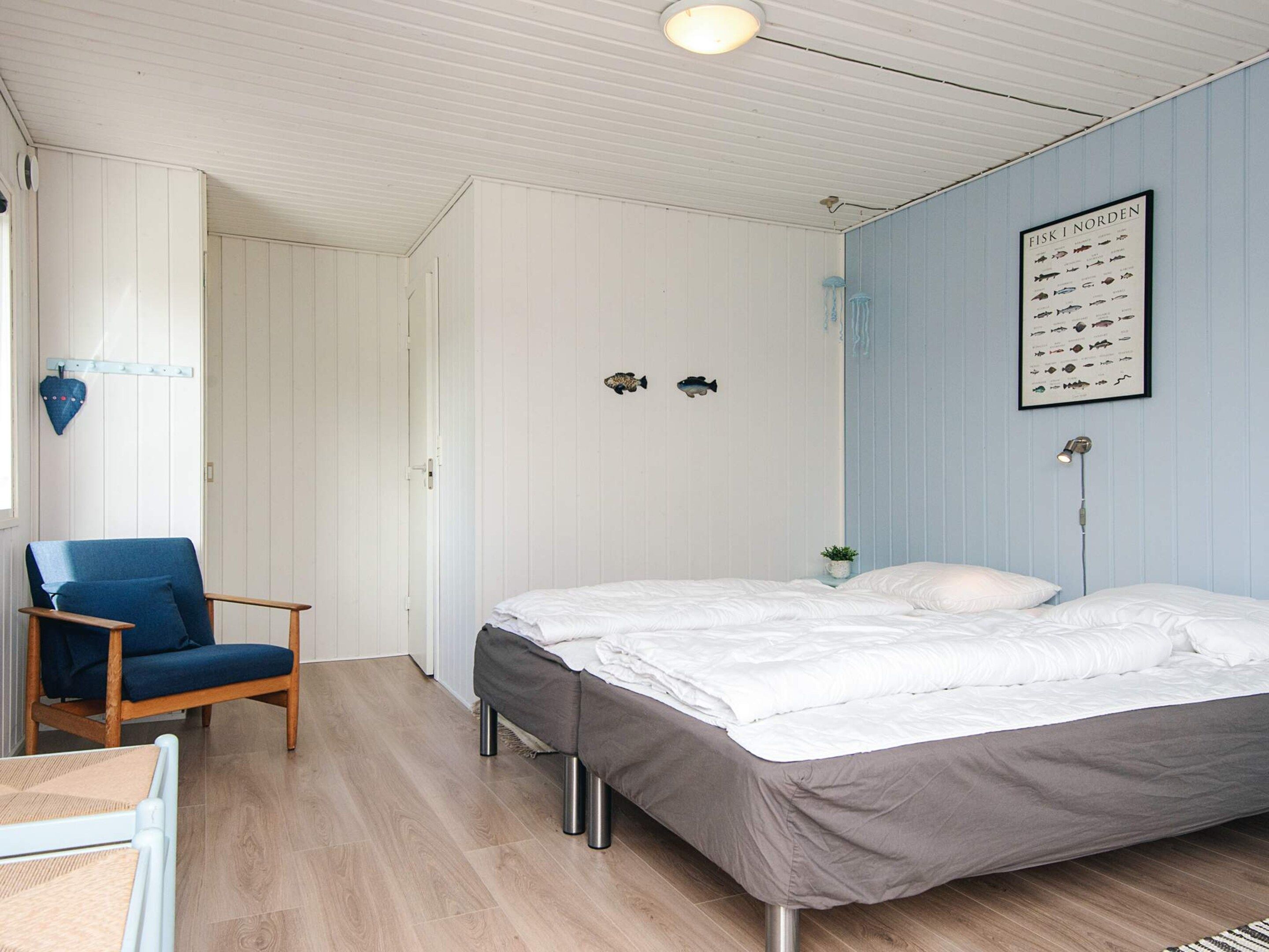 Une chambre à coucher comprenant un lit, une chaise, un tableau illustrant différentes espèces de poissons accroché au mur et un luminaire au plafond.