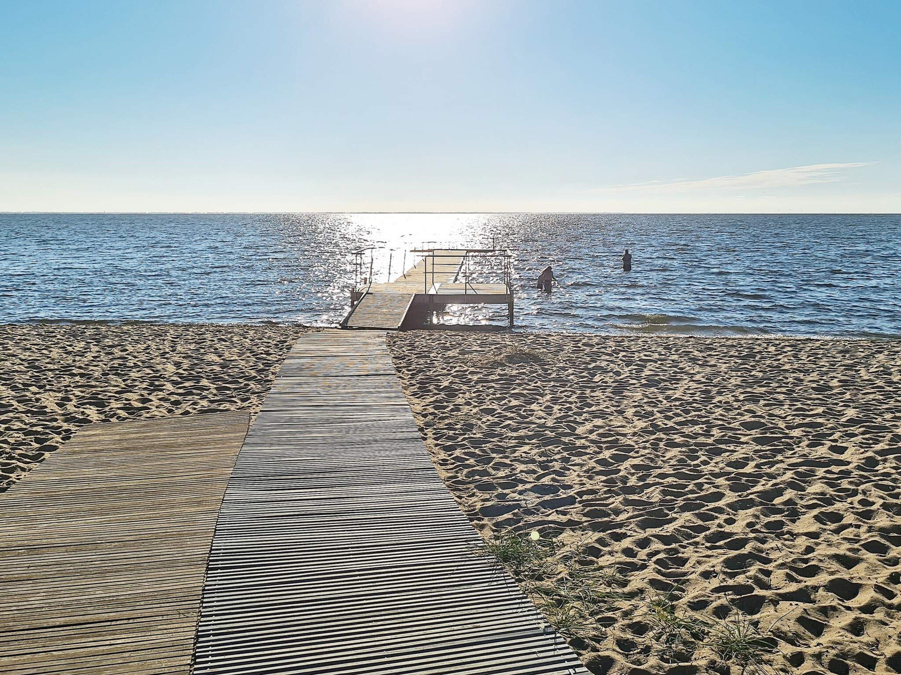 A wooden pier leading to a beach with clear skies.