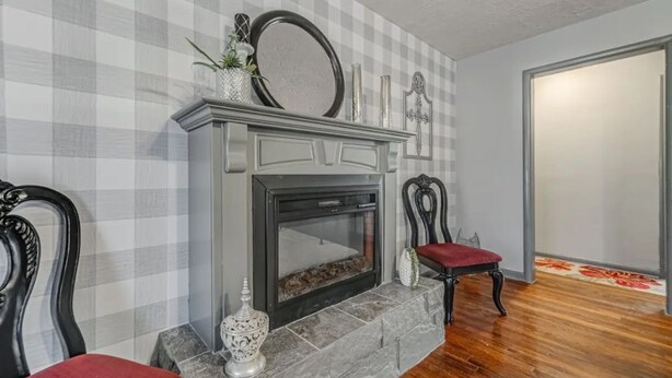 A room with a fireplace, two chairs, a checkered wall, and a wooden floor.