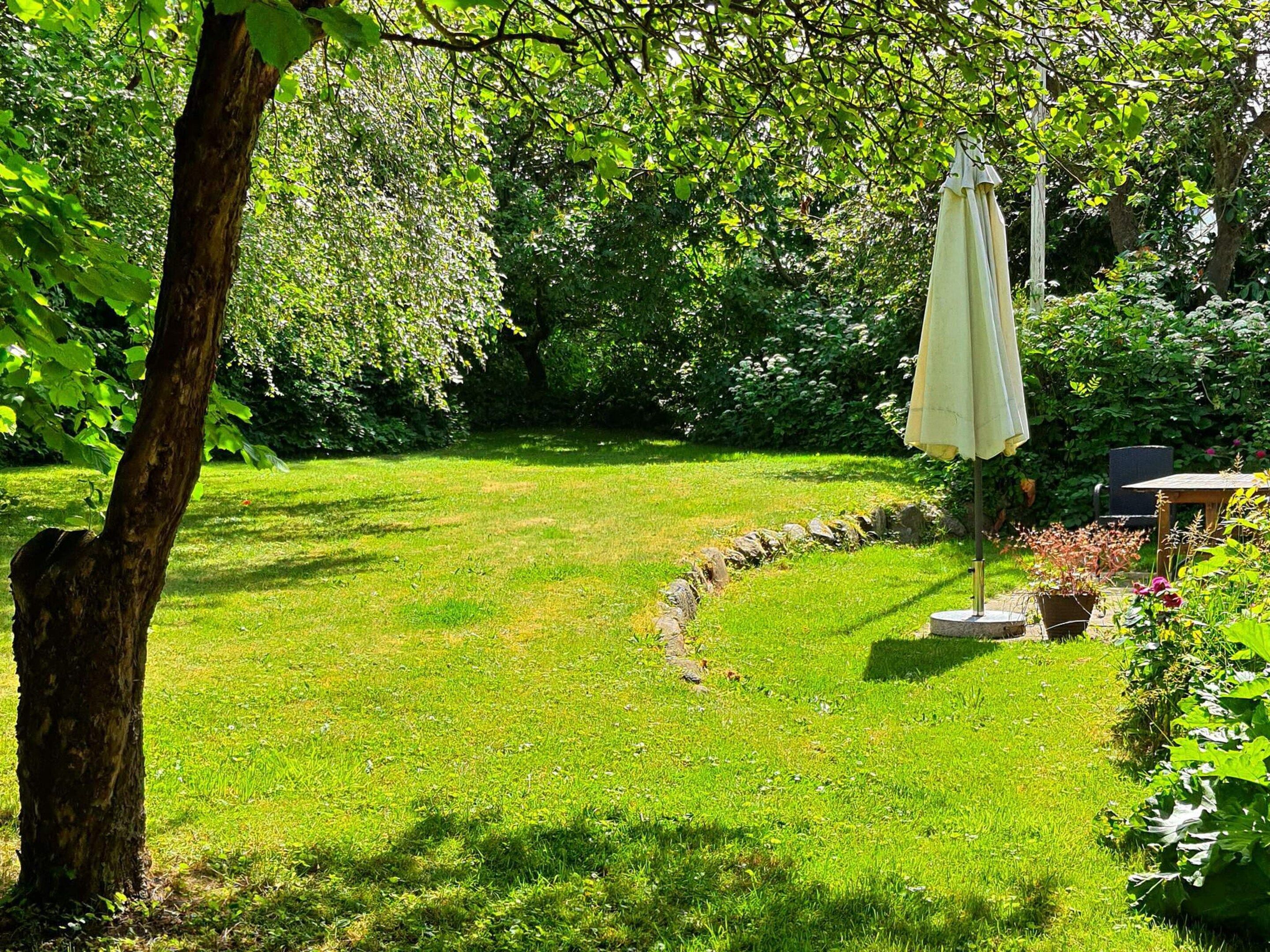 A grassy garden area with a stone pathway, a table, and an umbrella.