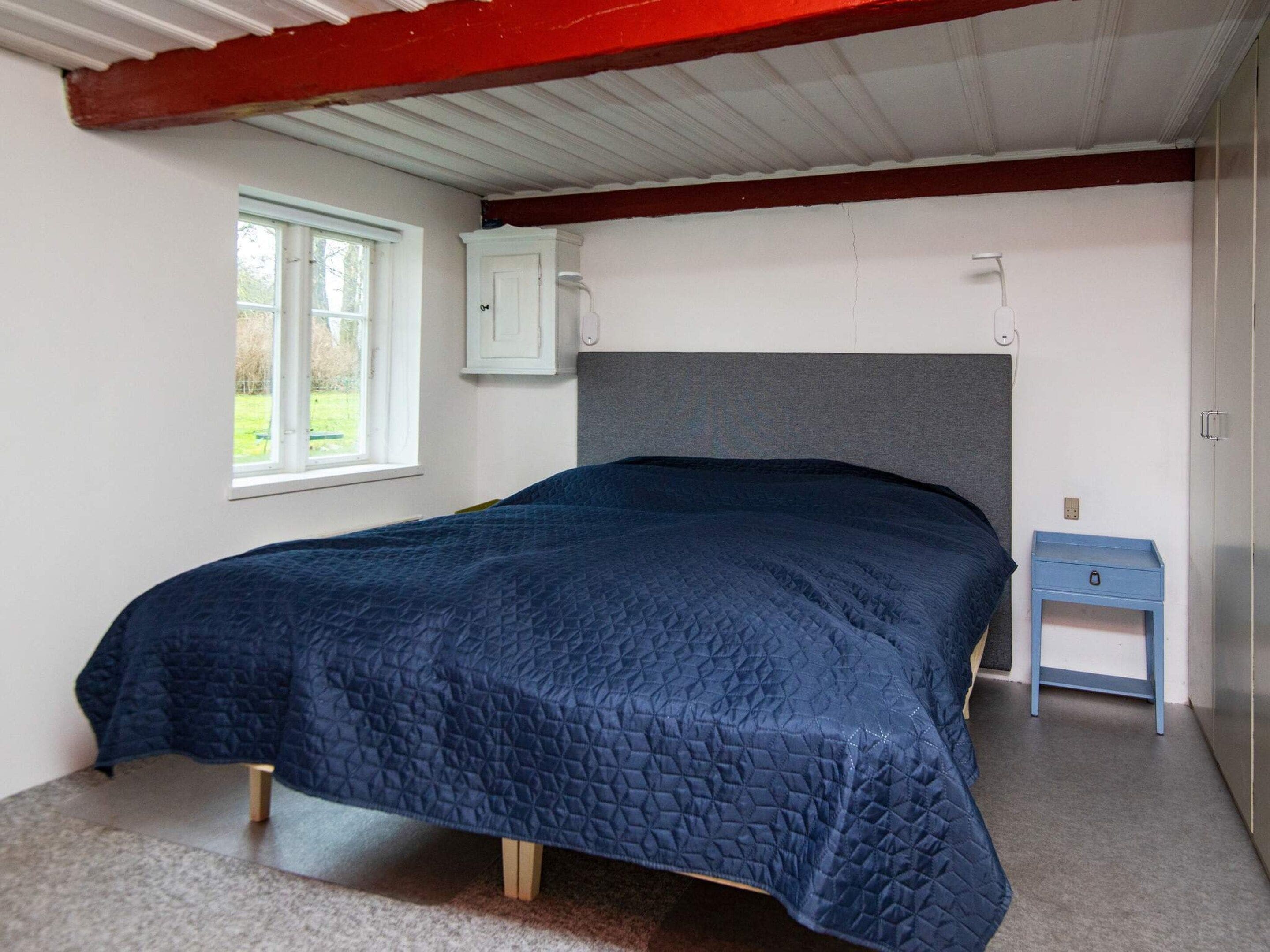 A bedroom with a bed, a window, a bedside table, and a wardrobe.