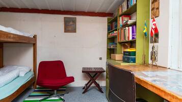 Ein Schlafsaalzimmer mit Etagenbetten, einem roten Stuhl, einem Schreibtisch mit Computer und einem Bücherregal.