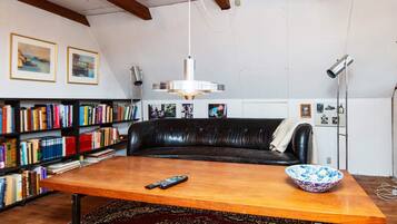 Ein Zimmer mit einer schwarzen Ledersofa, einem Holztisch, einem gemusterten Teppich und Bücherregalen voller Bücher.