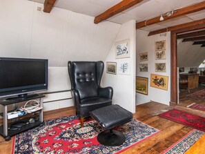 Ett vardagsrum med en svart läderfåtölj, en tv på ett tv-bord och en röd, mönstrad matta.
