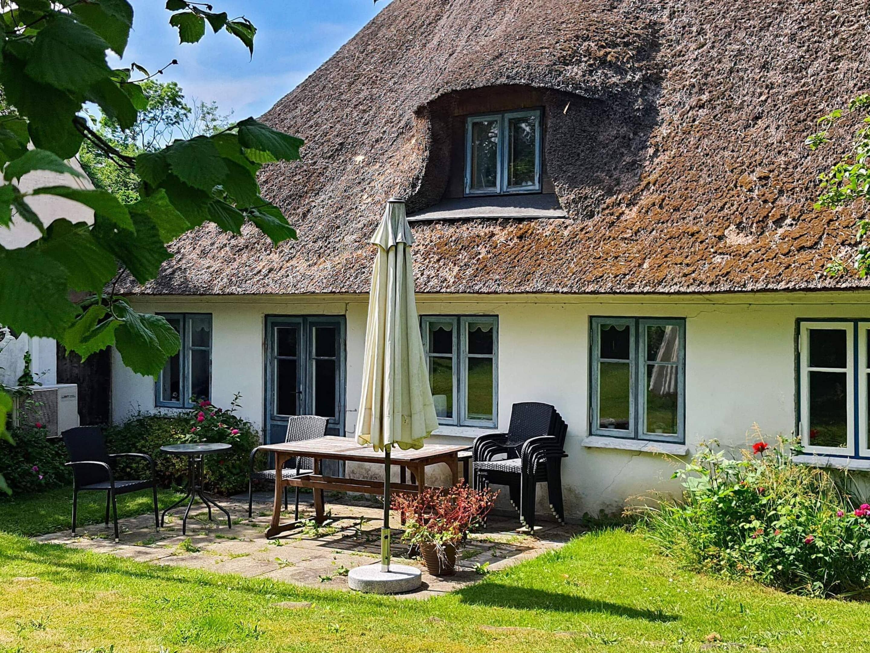 Ein Haus mit Strohdach, einer Terrasse, Sitzgelegenheiten im Freien und einem Garten.