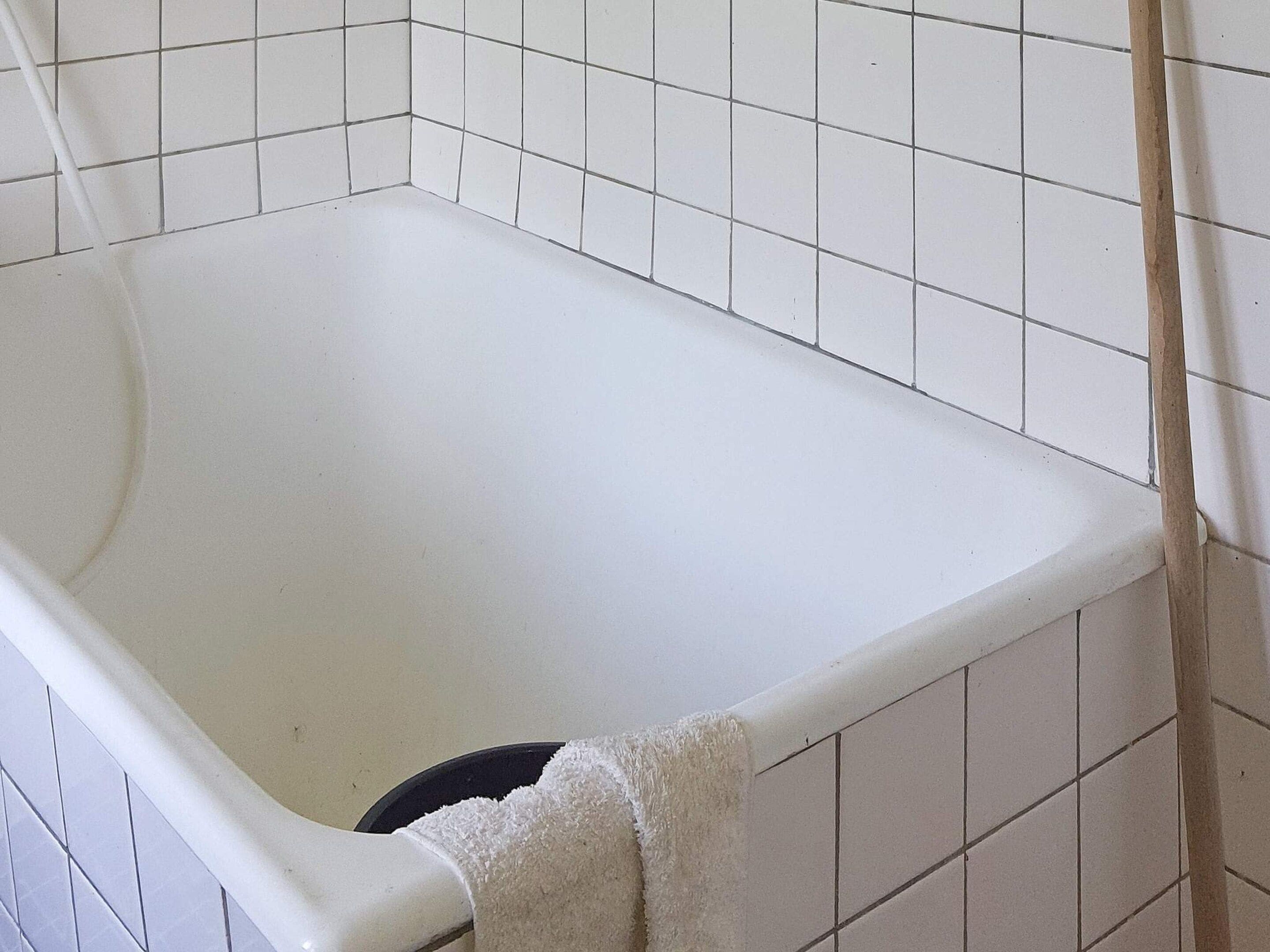 A white bathtub with a black drain, surrounded by white tiles.