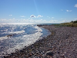 Ein felsiger Strand mit Wellen, blauem Himmel und weiter Küste.