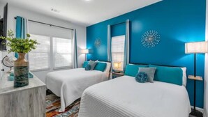 Une chambre d’hôtel avec deux lits, une grande fenêtre, un mur d’accent bleu et un miroir décoratif.