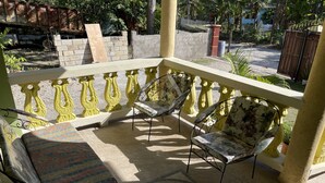 Un balcone con due sedie e un tavolo, ringhiera gialla e vista su una strada e del verde.