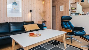 A cozy cabin interior with a wooden interior, a black leather sofa, a white coffee table, and a blue leather chair. - 6 Person Holiday Home in Ebeltoft (Ebeltoft)