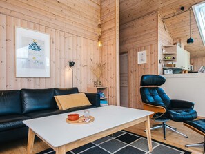 A cozy cabin interior with a wooden interior, a black leather sofa, a white coffee table, and a blue leather chair. - 6 Person Holiday Home in Ebeltoft (Ebeltoft)