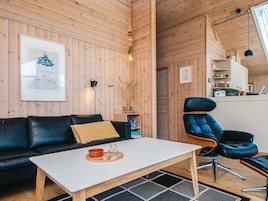 Un acogedor interior de cabaña con paredes de madera, un sofá de cuero negro, una mesa de centro blanca y un sillón de cuero azul.
