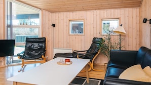 A room with wooden walls, a white table, a black leather sofa, and two leather chairs. - 6 Person Holiday Home in Ebeltoft (Ebeltoft)
