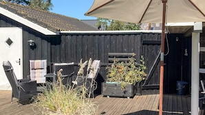 Eine Holzterrasse mit Gartenmöbeln, einem großen Sonnenschirm und einem Blumentopf.