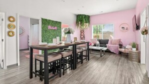 Ett modernt vardagsrum med en matplats, rosa väggar och en grön vägg med en skylt som säger ”Välkommen”.