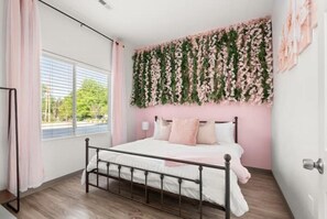 Een slaapkamer met een bed, een raam met gordijnen en een wand met beplante decoratie.