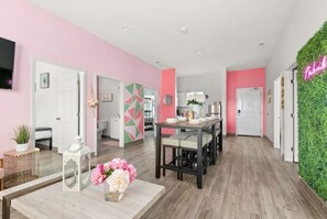 Een modern interieur met een roze en witte kleurenschema, een eethoek met een lange tafel, en een groene wanddecoratie.