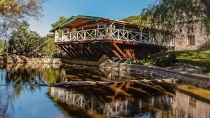 Uma ponte de madeira sobre um rio calmo, com um edifício de pedra ao fundo.
