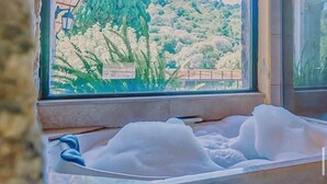 Quarto com uma grande janela com vista para uma paisagem montanhosa, uma banheira cheia de espuma e teto de madeira.