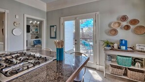 Una cocina moderna con estufa a gas, una mesa de comedor de vidrio y vistas al jardín trasero a través de puertas de cristal.