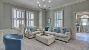 Un salón amplio con dos sofás color beige, un sillón azul y una mesa de centro.