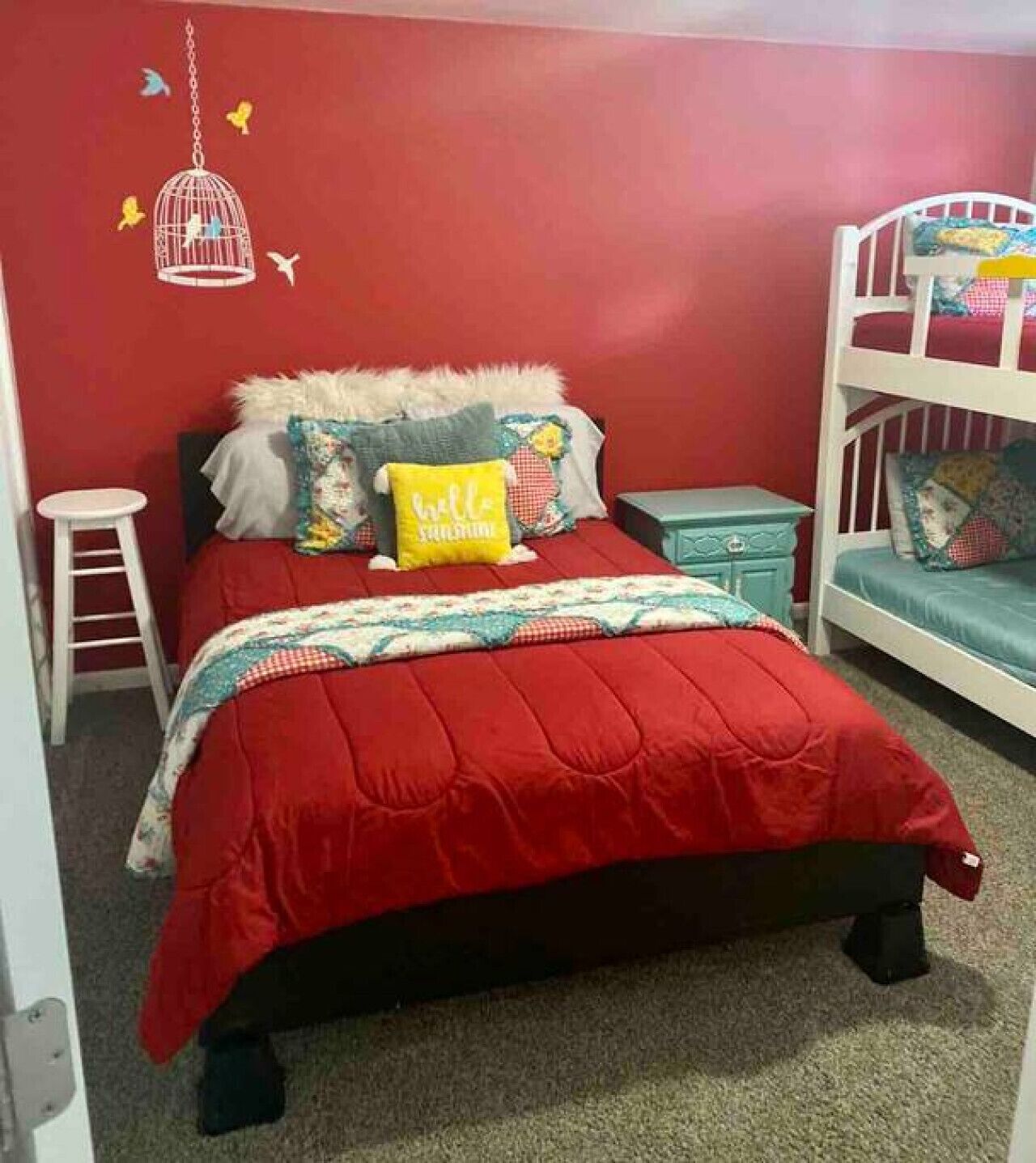 A bedroom with a red bedspread, a white headboard, and a bunk bed with a blue mattress.