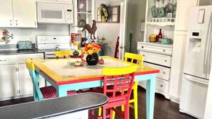 Una cocina con armarios blancos, una mesa de comedor con sillas coloridas y un refrigerador.