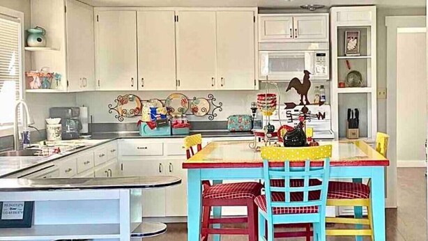 Una cocina con armarios blancos, una isla central y un comedor con mesa y sillas.
