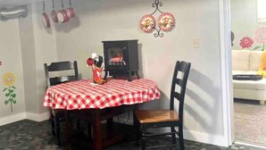 A dining area with a checkered tablecloth, two chairs, a small table with a decorative item, and wall decorations including a sunflower and two circular wall hangings. - The Checkered Daisy Cottage: Colorful and Fun (Price)
