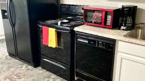 A kitchen with a black refrigerator, a black stove, a red microwave, and a dishwasher. - The Checkered Daisy Cottage: Colorful and Fun (Price)