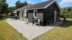 A small, dark-colored cabin with a tiled roof, a patio with outdoor seating, and a garden area. - 6 Person Holiday Home in Hojby-by Traum (Hojby)